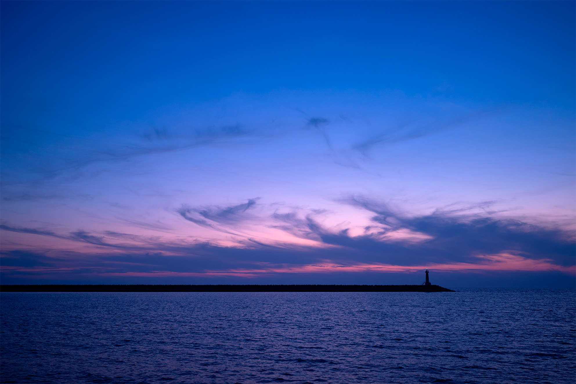 Svetionik na horizontu tokom plavog sata iznad mirnog mora